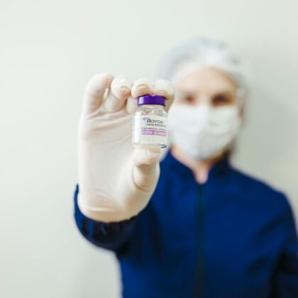 Healthcare worker holding a Botox vial in a clinical setting, wearing protective gear.