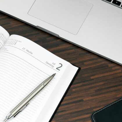 Open planner with a pen and laptop on a wooden desk, ready for organization.